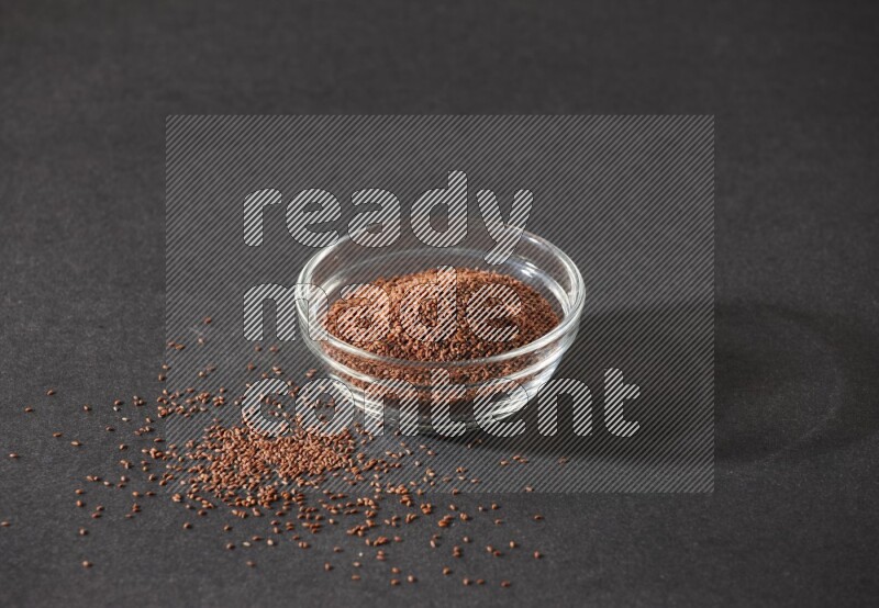 وعاء زجاجي ممتلئ ببذور حب الرشاد محاط بالبذور على أرضية سوداء