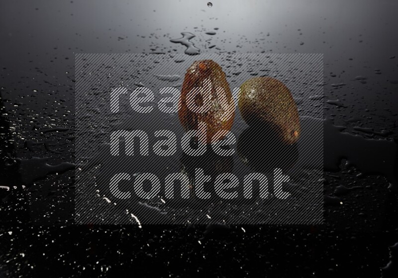 A whole avocado on black background with water drops.