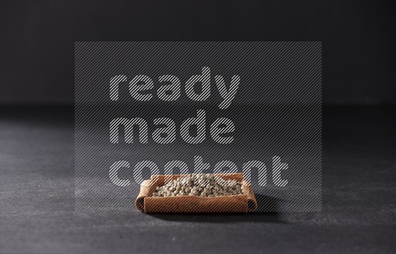 A single square of cinnamon sticks full of white pepper on black flooring