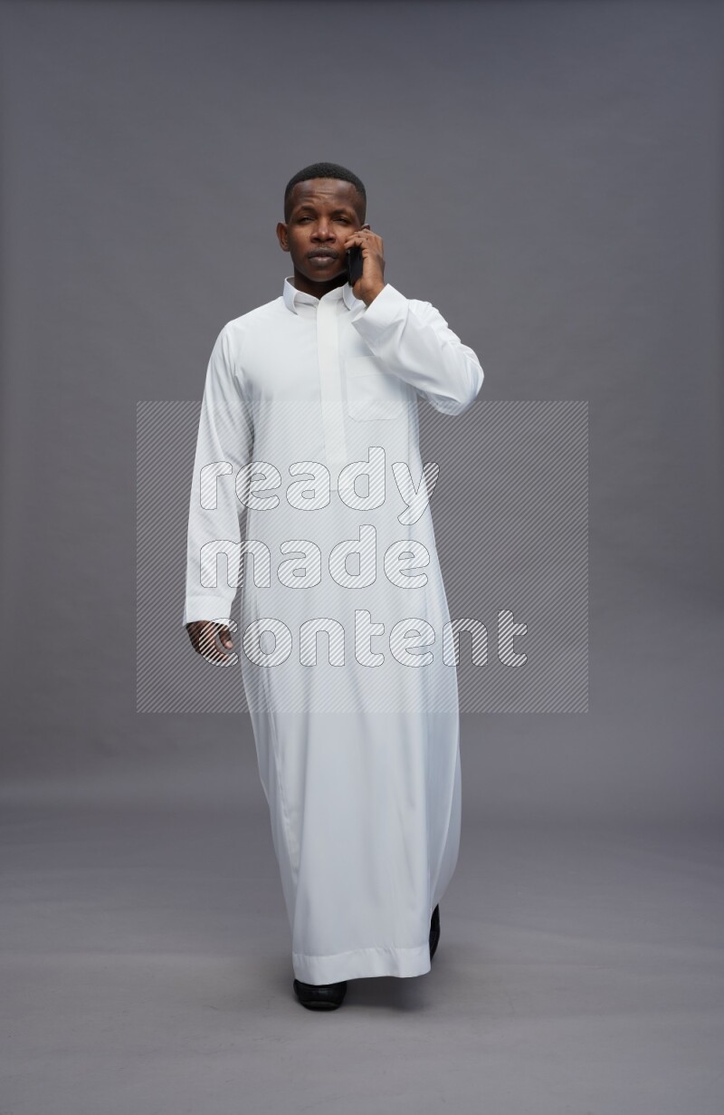 Saudi man wearing thob standing talking on phone on gray background