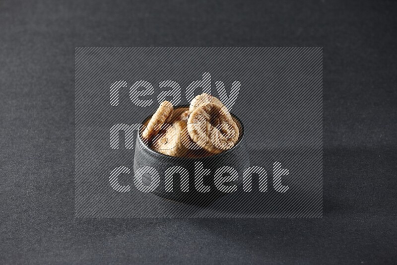 A black pottery bowl full of dried figs on a black background in different angles