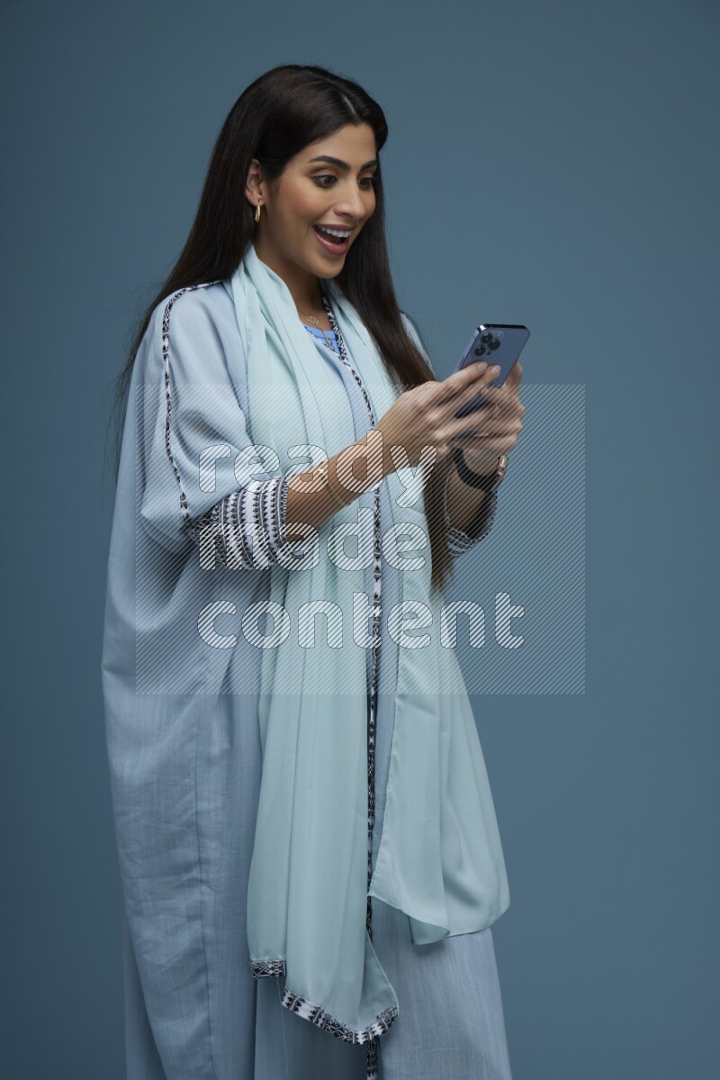 A Saudi woman Texting in a blue background wearing blue Abaya with no hijab