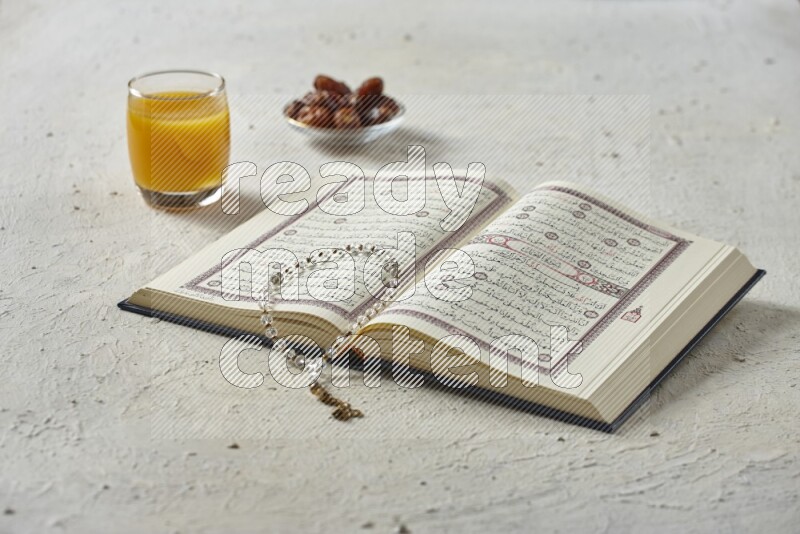 Quran with dates, prayer beads and different drinks all placed on textured white background