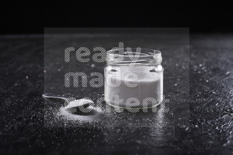 A glass jar full of fine table salt on black background