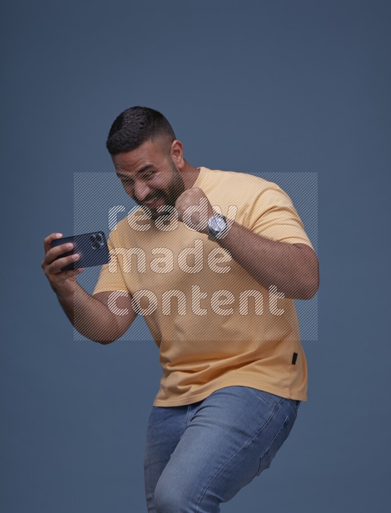 A man Playing Games on Smartphone on Blue Background wearing Orange T-shirt