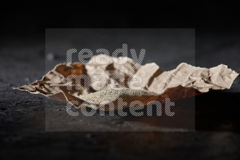 White pepper powder in a crumpled paper on textured black flooring