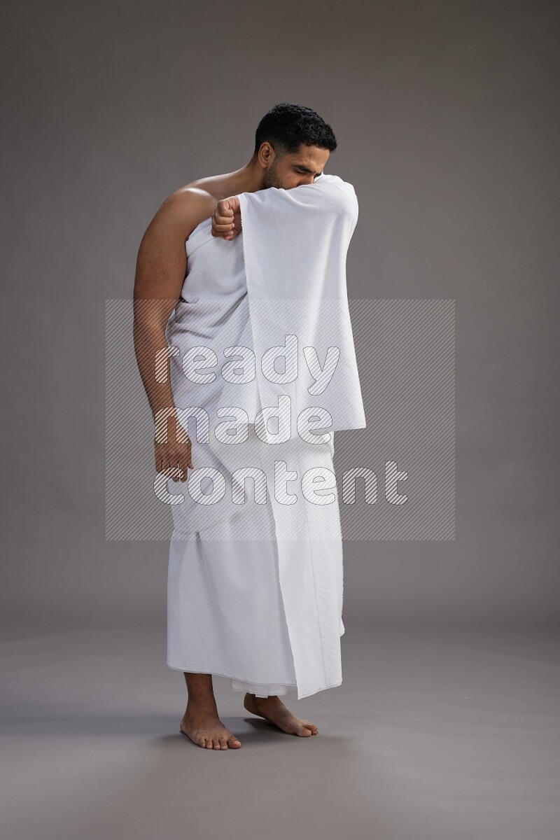 A man wearing Ehram standing showing how to sneeze on gray background
