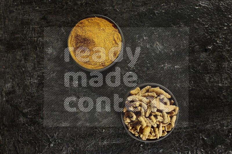 وعاءان من الفخار باللون الأسود، أحدهما ممتلئ ببودرة الكركم والآخر ممتلئ بأصابع كاملة من الكركم المجفف على خلفية سوداء