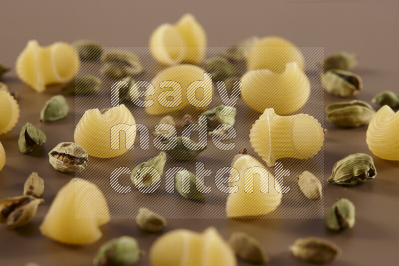 Raw pasta with different ingredients such as cherry tomatoes, garlic, onions, red chilis, black pepper, white pepper, bay laurel leaves, rosemary and cardamom on beige background
