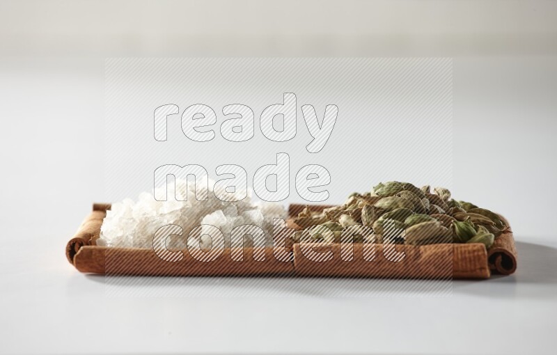 2 squares of cinnamon sticks full of cardamom and white salt on white flooring