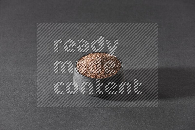 وعاء فخاري أسود ممتلئ بحبوب بذر الكتان على أرضية سوداء