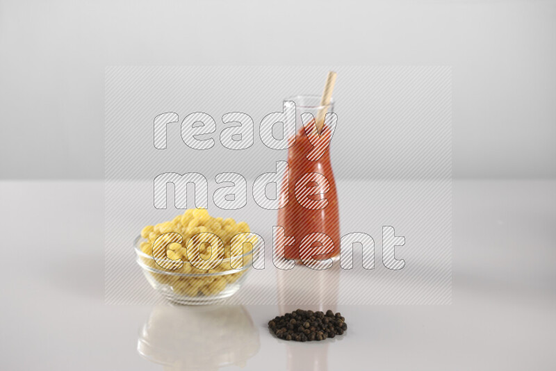 Raw pasta with tomatoe pasta with different ingredients such as cherry tomatoes, basil, garlic, bay laurel, cardamom, white pepper, black pepper, red chilis and wheat stalks on light grey background