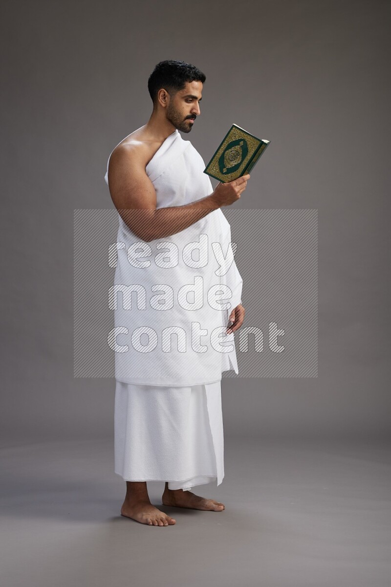 A man wearing Ehram Standing reading quran on gray background