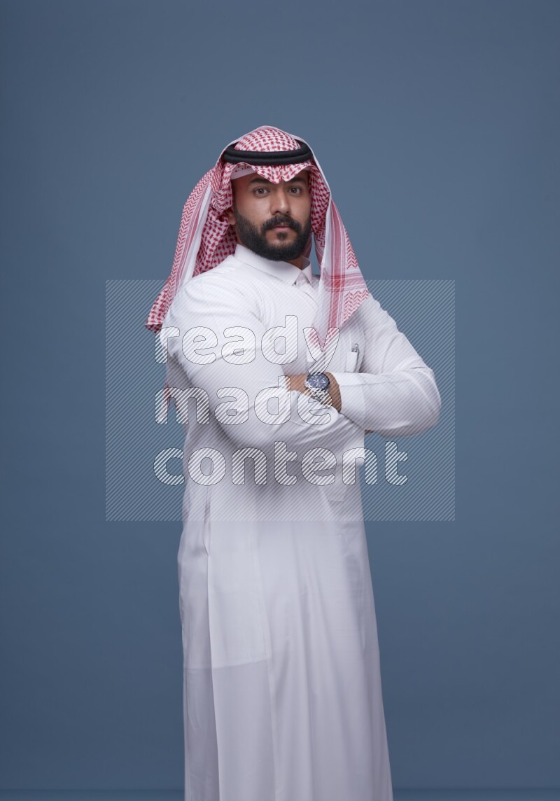 A Saudi man posing on blue background wearing Thob and Shomag