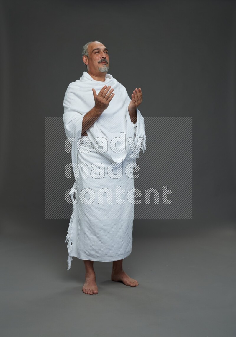 A man wearing Ehram Standing dua'a on gray background