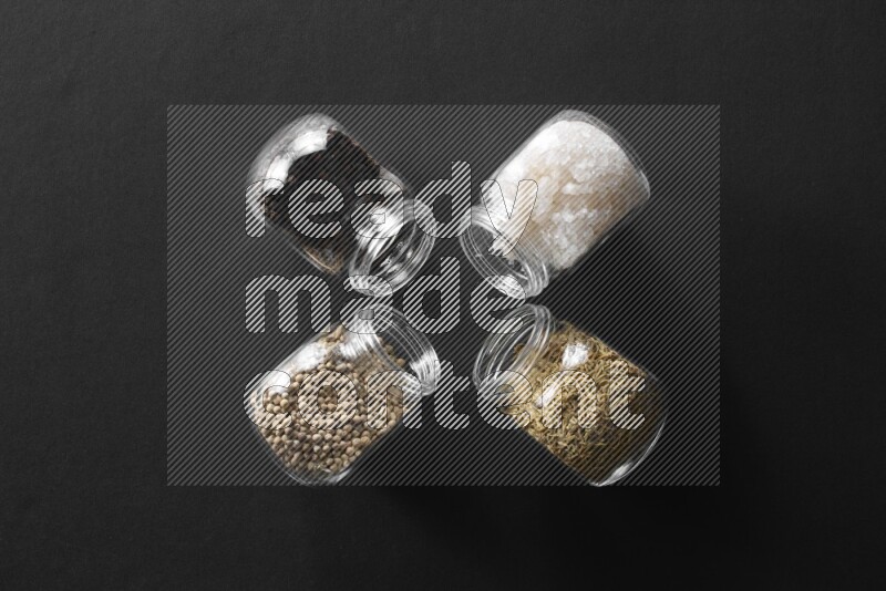 ملح وفلفل أسود وفلفل أبيض وكمون في أوعية زجاجية علي خلفية سوداء