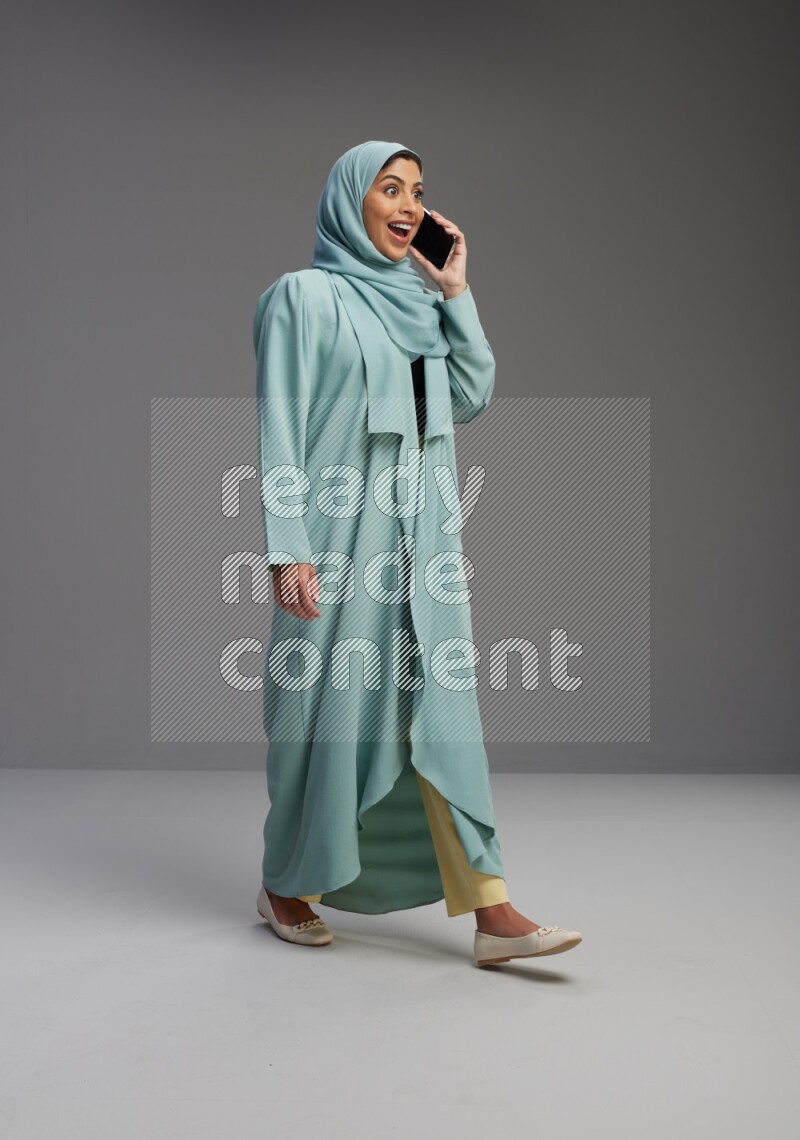 Saudi Woman wearing Abaya standing talking on phone on Gray background