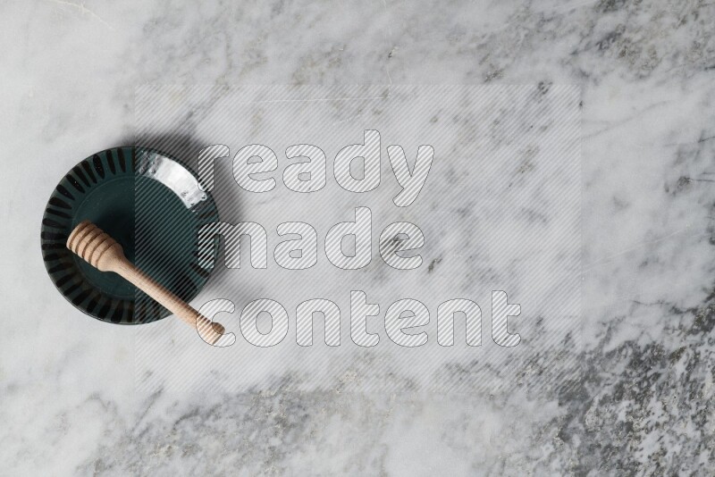 Multicolored pottery plate with wooden honey dipper in it on grey marble background
