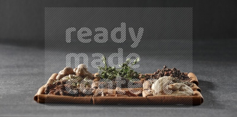 9 مربعات من أعواد القرفة ممتلئة بالشاي في المنتصف محاطة بجوزة الطيب والنعناع المجفف والقرنفل والريحان المجفف والزنجبيل المجفف والقرفة واليانسون والهيل على أرضية سوداء