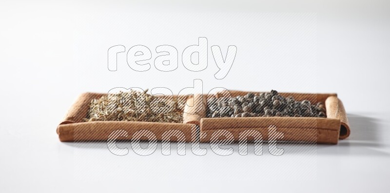 مربعان من أعواد القرفة ممتلئان بحبوب الفلفل الأسود وحبوب الكمون علي خلفية بيضاء