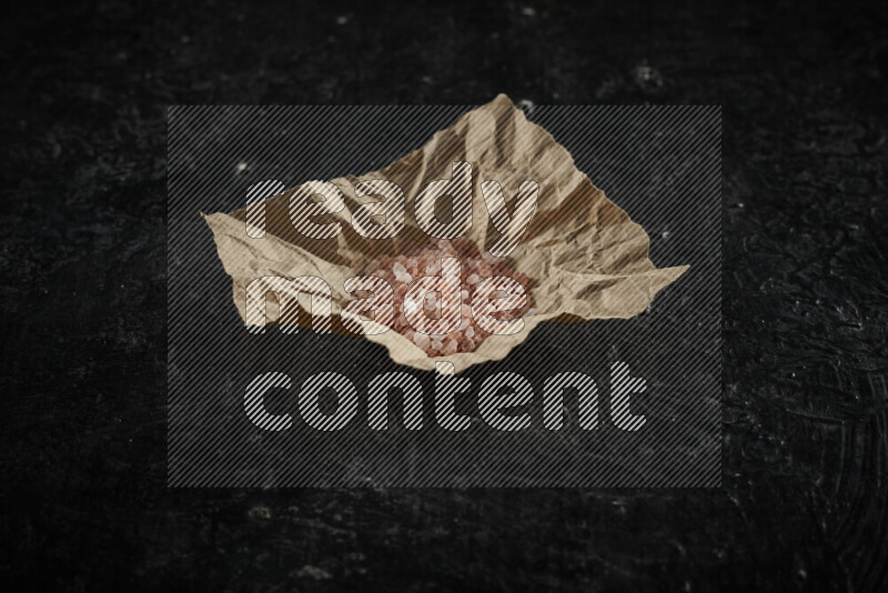 A crumpled piece of paper full of pink himalayan salt on black background