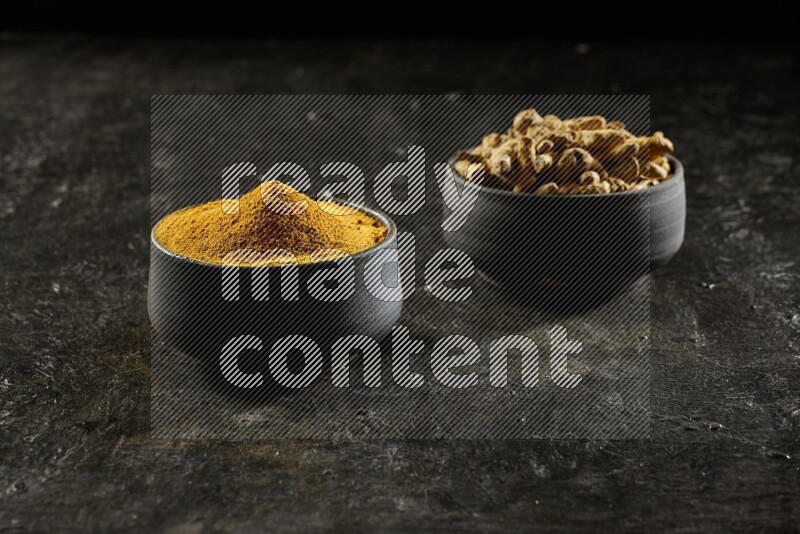 وعاءان من الفخار باللون الأسود، أحدهما ممتلئ ببودرة الكركم والآخر ممتلئ بأصابع كاملة من الكركم المجفف على خلفية سوداء