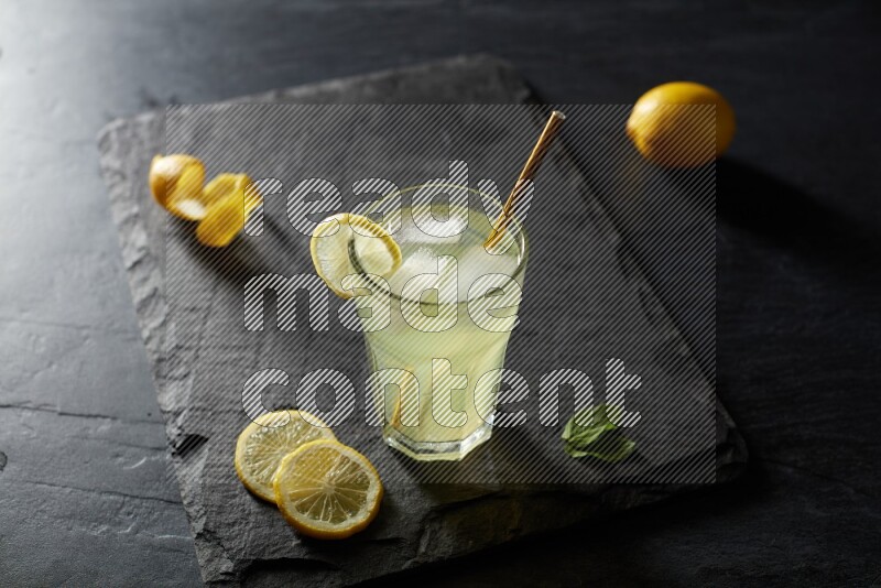 A glass of lemon juice with a straw on black background