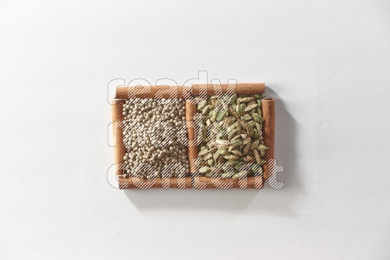 مربعان من أعواد القرفة ممتلئان بحبوب الهيل وحبوب الفلفل الأبيض علي خلفية بيضاء