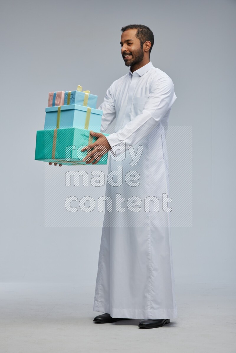 Saudi man Wearing thob standing holding gift box on Gray background