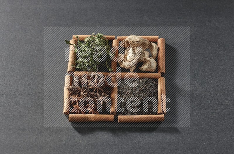 4 squares of cinnamon sticks full of black tea, dried ginger, dried mint leaves and star anise on black flooring