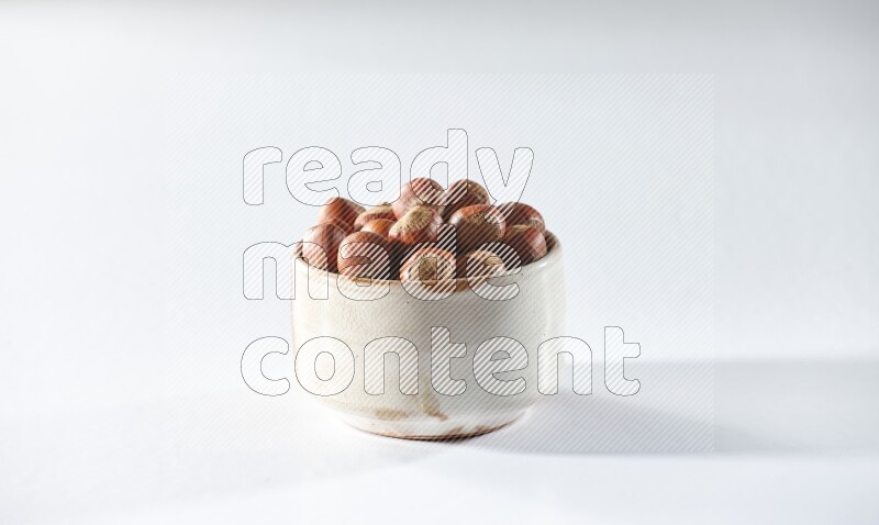 A beige ceramic bowl full of hazelnuts on a white background in different angles