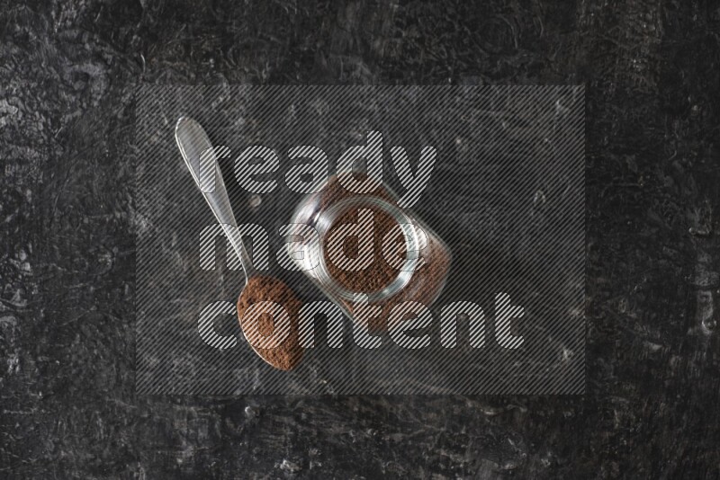 وعاء زجاجي للبهارات وملعقة معدنية ممتلئان ببودرة القرنفل على أرضية سوداء