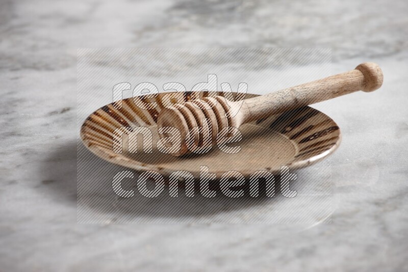 Multicolored pottery plate with wooden honey dipper in it on grey marble background