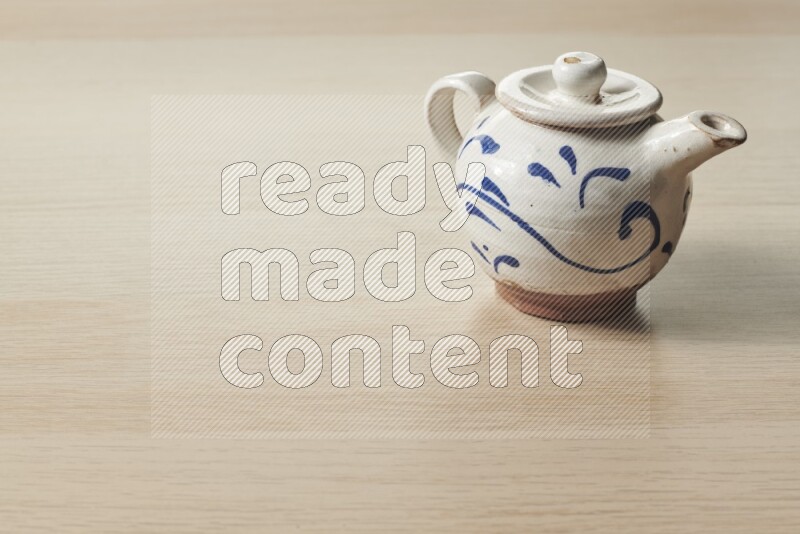 A pottery teapot on light wooden background