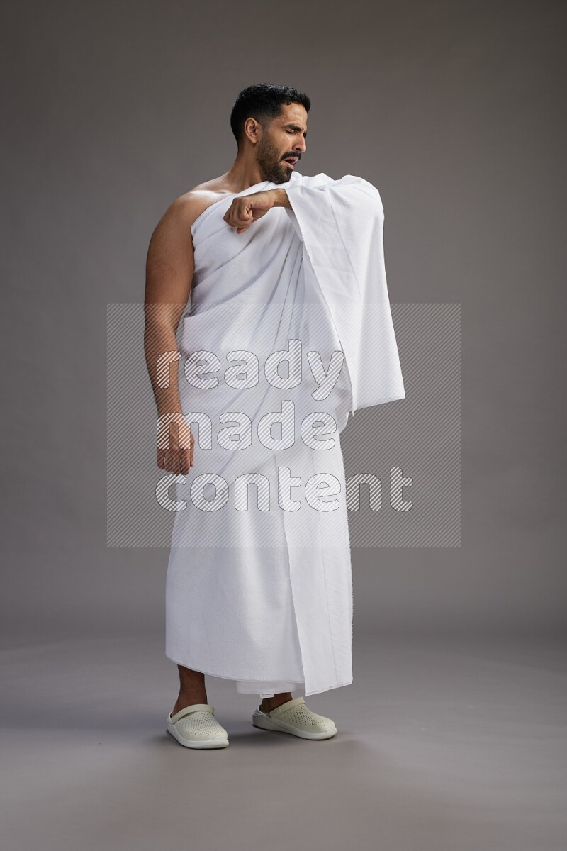 A man wearing Ehram standing showing how to sneeze on gray background