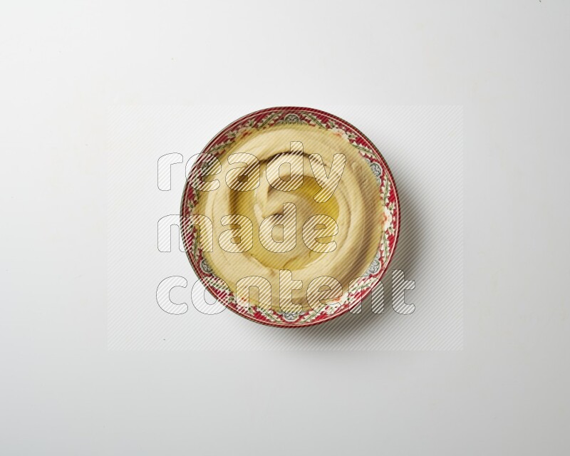 Hummus in a red plate with patterns garnished with olive oil on a white background