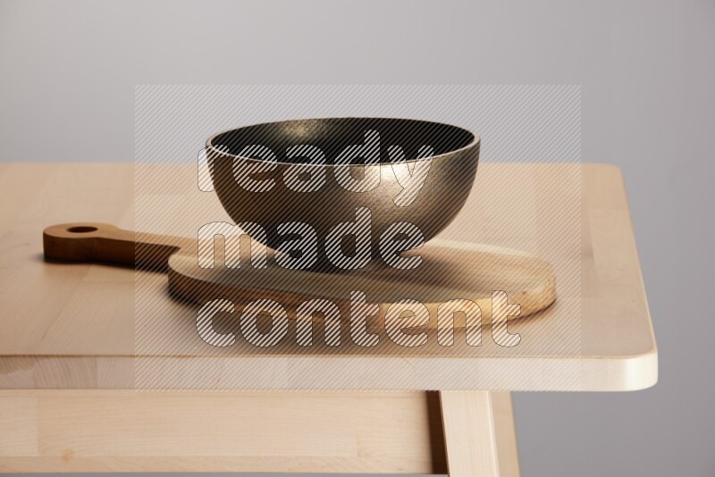 brass bowl placed on a  wooden oval cutting board on the edge of wooden table