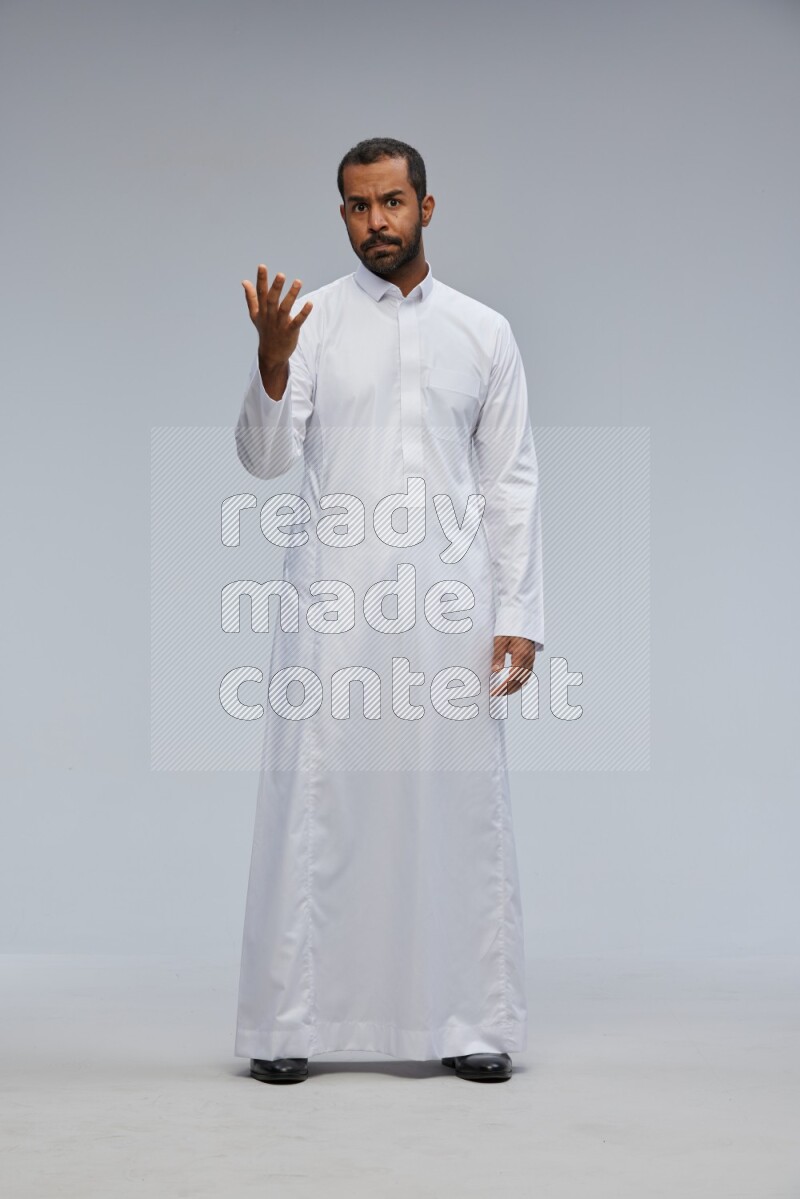 Saudi man Wearing Thob standing interacting with the camera on Gray background