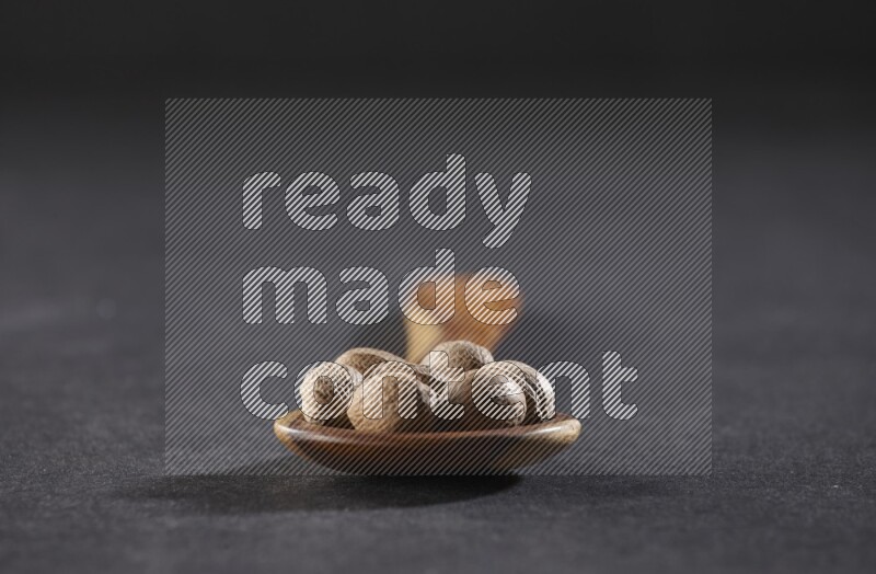 ملعقة خشبية كبيرة مليئة بحبوب جوزة الطيب الكاملة على خلفية سوداء