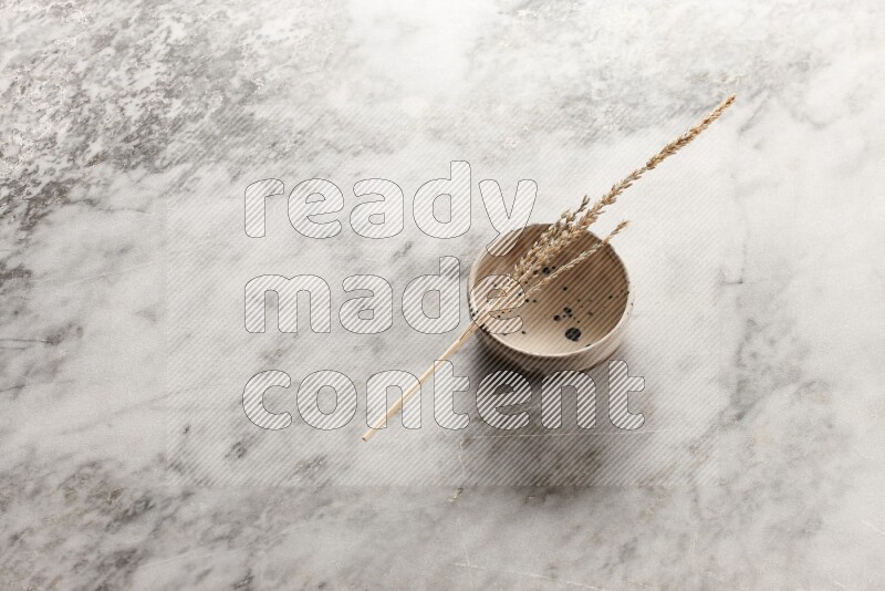 Wheat stalks on multicolored pottery bowl on grey marble background