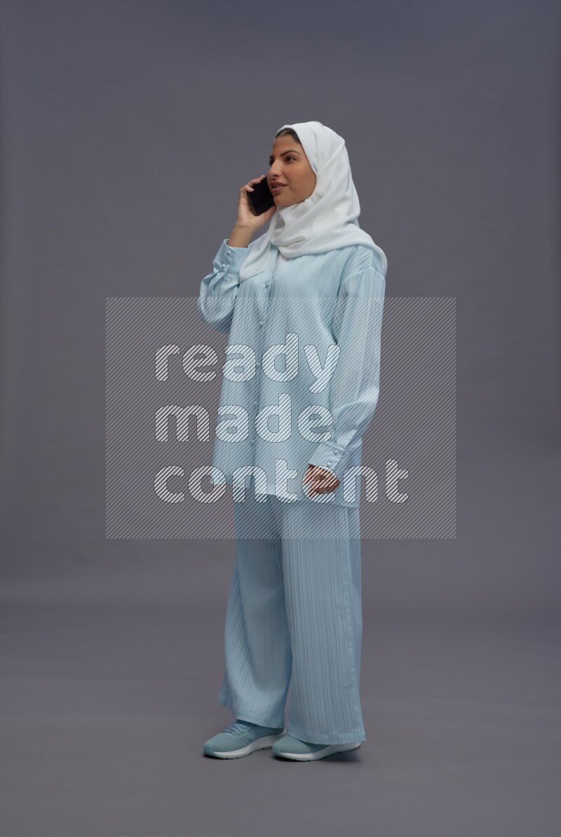 Saudi woman wearing hijab clothes standing talking on phone on gray background