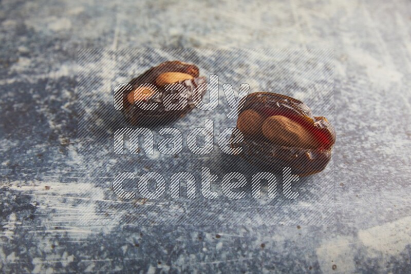 two almond stuffed madjoul dates on a rustic blue background