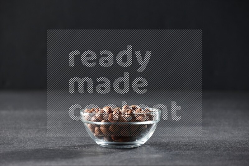 A glass bowl full of peeled hazelnuts on a black background in different angles