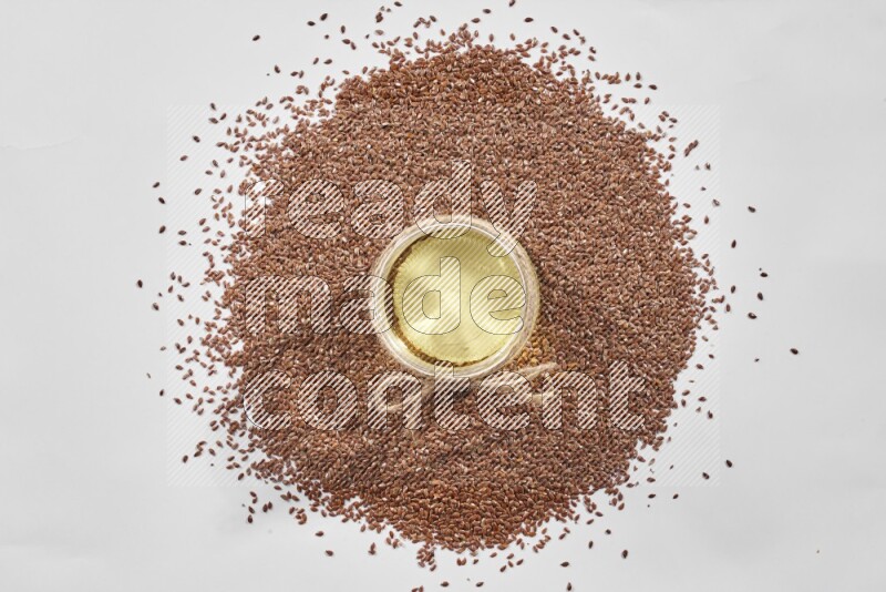 A glass jar full of flaxseeds oil surrounded by flax seeds on a white flooring