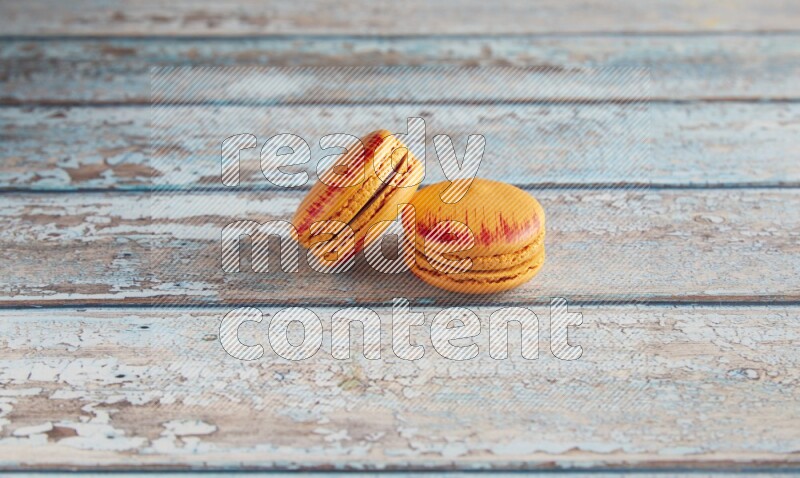 45º Shot of two orange Exotic macarons on light blue wooden background