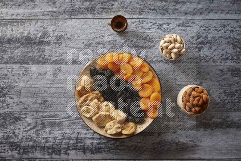 Dried fruits in a pottery plate with nuts and coffee in a dark setup