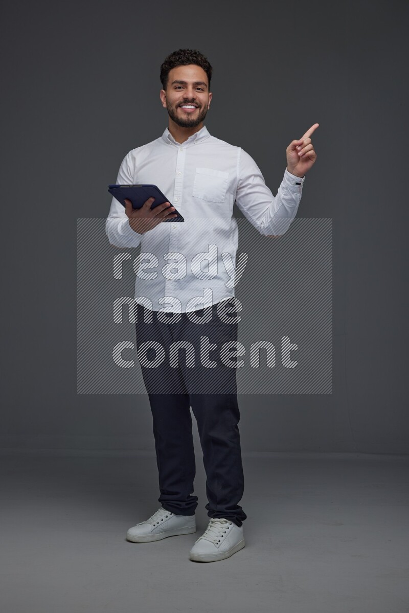 A man wearing smart casual standing and using his tablet and making multi hand gestures eye level on a gray background