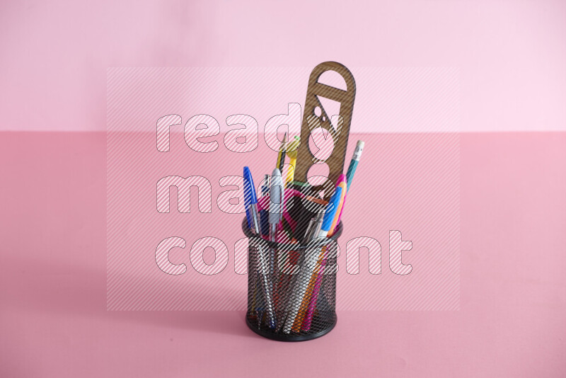 Pens, pencils and other different school supplies in a metal pen holder on rose background