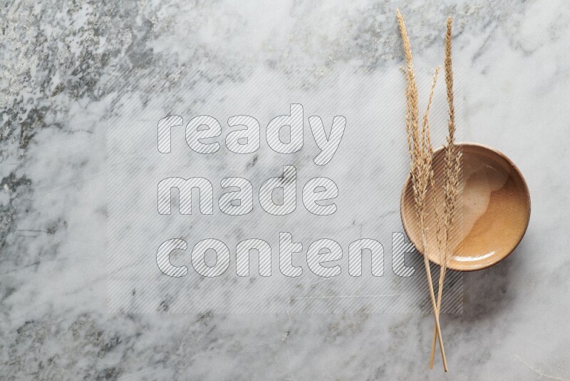 Wheat stalks on multicolored pottery plate on grey marble background