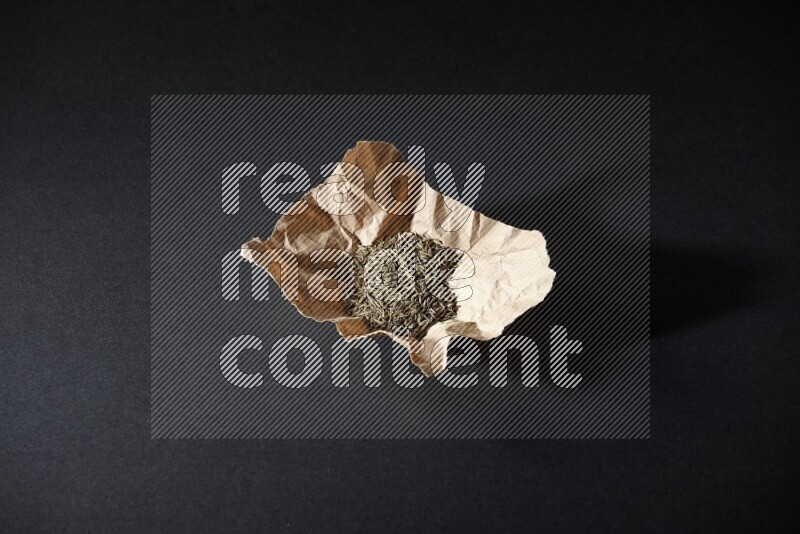 Cumin seeds in a crumpled piece of paper on black flooring